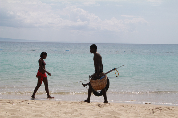 Spearfisherman and bikini clad woman walking on beach